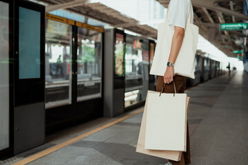 Man in white shirt holding paper shopping bag on sky train platform.