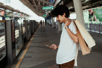 Side view - Man with shopping paper bag using smartphone on train platform.