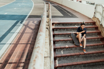 Skateboard player woman using smartphone sitting on stair.