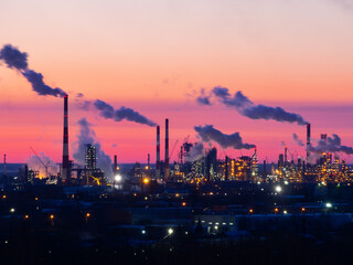 Obraz na płótnie Canvas Refinery at sunset. Pipes of a thermal power station and an oil refinery, illuminated plant installations on a red sunset sky. Blue smoke from pipes of an oil refinery and plastic