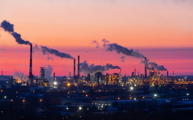 Obraz na płótnie Canvas Refinery at sunset. Pipes of a thermal power station and an oil refinery, illuminated plant installations on a red sunset sky. Blue smoke from pipes of an oil refinery and plastic