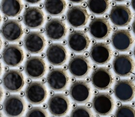 Metal grate with circular holes with dark background.  Dried autumn leaves on grate.