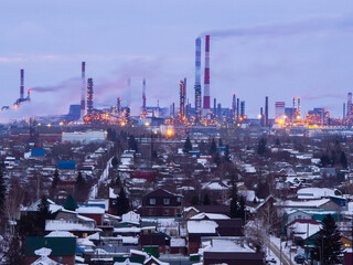 Omsk oil refinery at sunset with luminous lights. High pipe of a thermal power station near the refinery