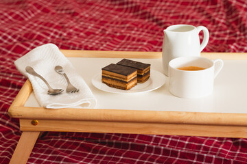 Cup of coffee with milk, and chocolate cake. Sweet delicious breakfast on a bed tray table
