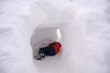 little frozen boy in winter jacket lying sleep on snow in big ice snowbank in mountains