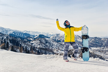 Young woman snowboarder in a yellow jacket and black helmet on the background of snowy mountains