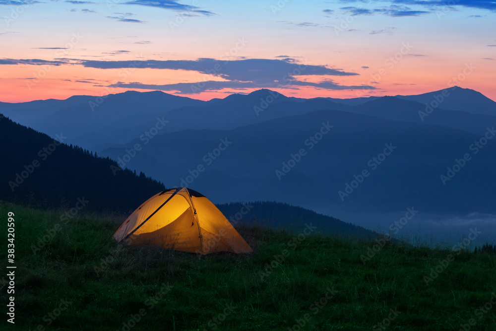 Wall mural orange tourist tent illuminated from inside on mountain