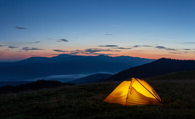 Orange luminous tent on the mountain in evening or early morning