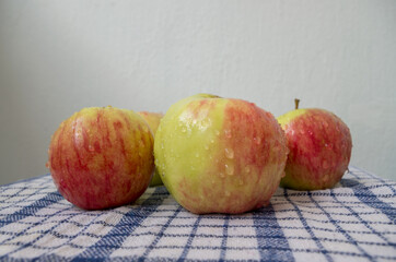 Small pile of freshly washed red-green apples, with water drops on the surface of the peel, lying picturesquely on a white waffle fabric textile tablecloth checkered with blue color stripes.