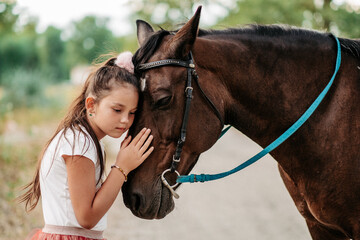 Obraz premium Friendship of a child with a horse. A little girl is affectionately stroking her horse. Walking girls with a horse in the park in autumn.