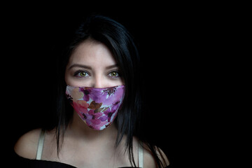 Young woman looking straight ahead, with flower mask and black background