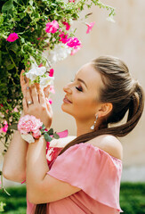 Fototapeta premium Cute girl in a pink dress sniffs flowers on the bushes