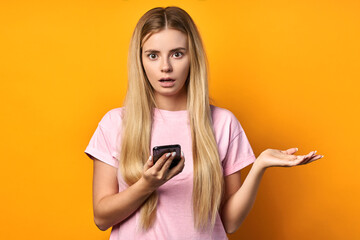 Naklejka premium Surprised pretty young woman in a pink T-shirt who opens her mouth. The blonde is shocked that she found in the application, found something interesting, sharing the news with you on the Internet