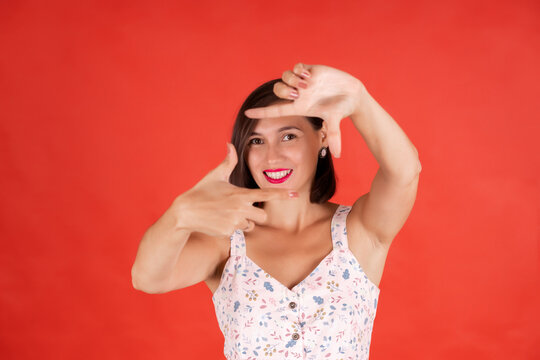 Young woman framing her face with her fingers on a red colored background
