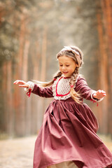 Little cute girl in a historical dress is walking in a pine forest