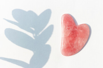 Pink massager gua sha and shadow on white background top view.