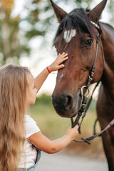 Obraz premium Friendship of a child with a horse. A little girl is affectionately stroking her horse. Walking girls with a horse in the park in autumn.