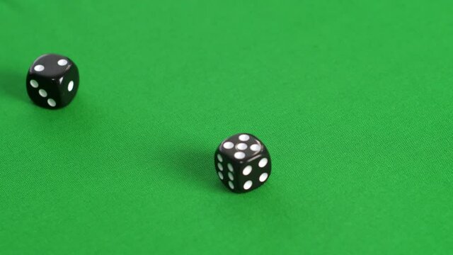 Close-up view of person playing with dice on green table. Cropped shot of player throwing black dice on green background
