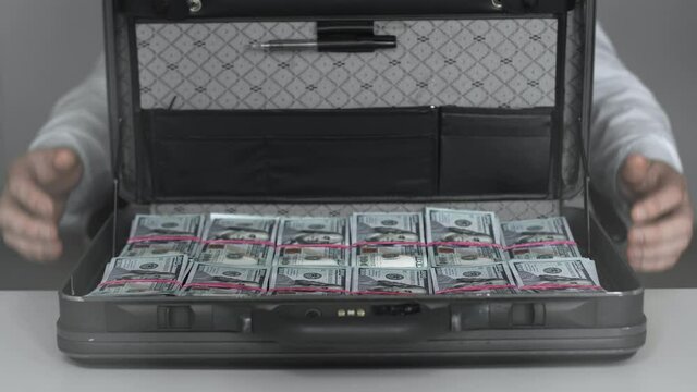 Businessman opens case full of cash dollars money. Bribe, corruption concept. Man in white shirt sits on the chair and turns around. Corruption concept. Greed person. Riches. Finance and investment