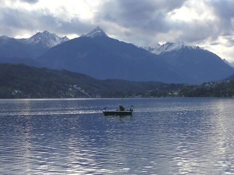 Lonesome Fisherman on Millstaetter Lake in the Alps with snowy mountains in October