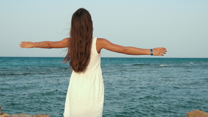 Fototapeta na wymiar Long hair young woman enjoying warm wind at seaside promenade at sea resort.