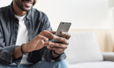 Male hands with smartphone at home closeup, young smiling man using mobile phone indoors
