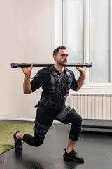 Muscular athletic man in EMS suit doing lunge exercise with fitness bar