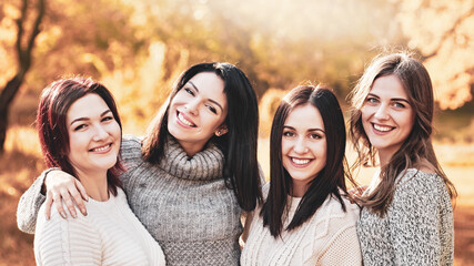 Fototapeta premium Portrait of four smiling best girlfriends posing in autumn forest