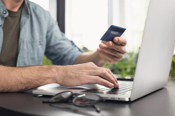 Obraz na płótnie Canvas Male hand holding credit card and using laptop in office. Business man or entrepreneur working. Online shopping, e-commerce, internet banking, spending money, working from home concept