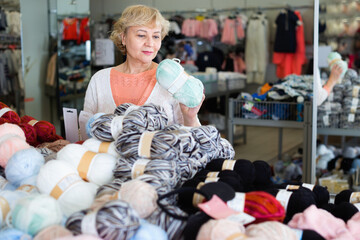 Fototapeta na wymiar Happy cheerful positive mature woman buyer choosing colored yarn for knitting on sale