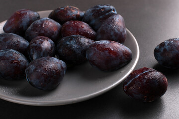 Fresh appetizing plums in a gray bowl, summer concept, copy space.