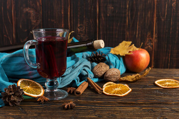 Cup of mulled wine with spices, bottle, scarf, dry leaves and oranges on a wooden table. Autumn mood, method to keep warm in the cold, copy space.