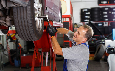 portrait of adult mechanic technician installing car wheel after repair of balancing at service...
