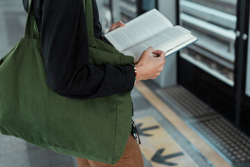 Close up hand of man reading a book at train station.