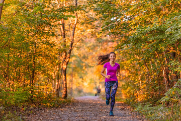 Trail running happy Asian woman jogging outdoors in autumn forest park. Fall weather with yellow foliage leaves.