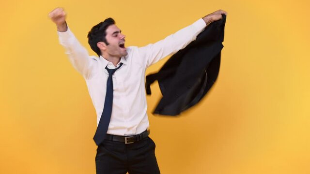 Joyful happy young Caucasian businessman with formal attire dancing and singing while holding blazer after work isolated on colorful studio yellow background