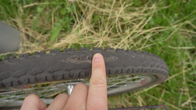 A cyclist inspects an old punctured tire on a bicycle wheel, outdoor