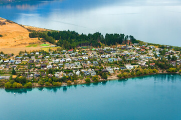 Amazing aerial view of residential suburb with villas on the shore of peninsula, surrounded by clear blue waters of Wakatipu lake near Queenstown, beautiful landscape of New Zealand