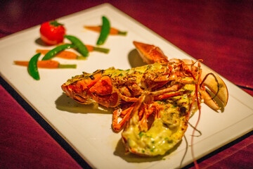 a whole grilled lobster with a  tomato, snow peas and baby carrots on the side