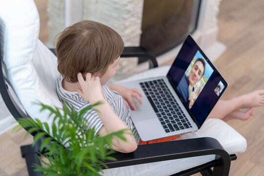 Happy kid boy sit on chair with computer using laptop having a video call with father. Child talking to his dad and dog on video chat