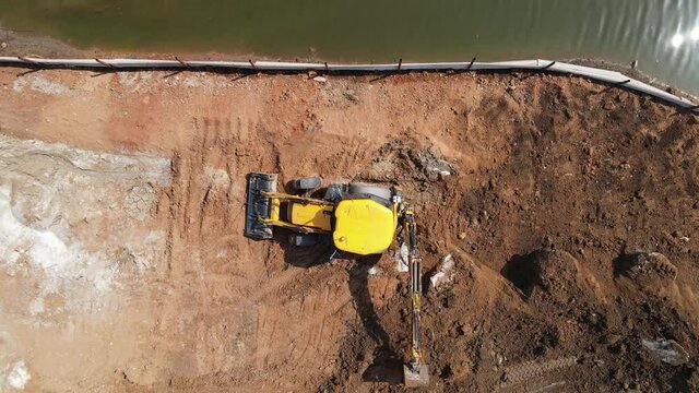 Aerial view of heavy machinery a rear actor, back actor working in construction site near the bank of a river, heavy equipment top down footage
