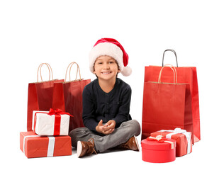Cute little boy in Santa hat, with gift boxes and shopping bags on white background