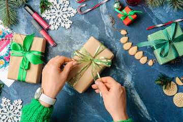 Hands with Christmas gift and cosmetics on color background