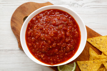 Homemade Tomato Salsa and Nachos on a rustic wooden board on a white wooden background, top view....