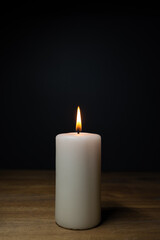 Fototapeta na wymiar A white burning candle on a wooden table, dark background and copy space