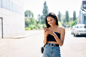 Obraz premium Happy smiling black woman looking at her smartphone walking in the city