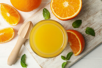 Board with glass of orange juice, oranges and juicer on wooden background