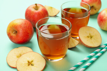Apple slices, straws and glasses of apple juice on mint background