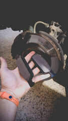 A man's hand with new brake pads on the background of a car without a wheel. Service work on replacing the front brake pads.