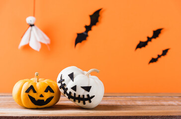 Funny Halloween day decoration party, Cute pumpkin ghost spooky jack o lantern face, black spider and bats on wooden table, studio shot isolated on an orange background, Happy holiday concept